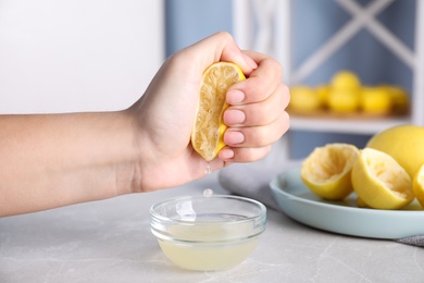 Woman squeezing lemon juice into glass bowl at grey marble table, closeup