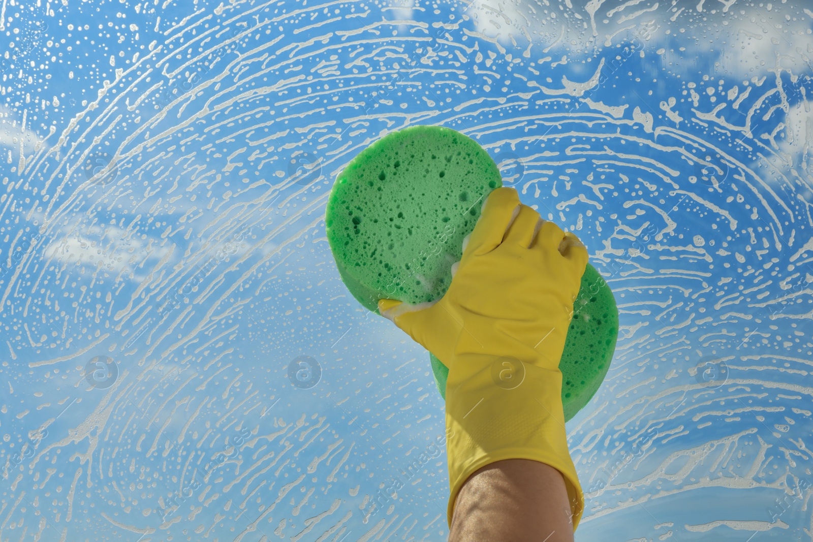 Photo of Woman cleaning glass with sponge indoors, closeup