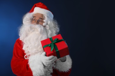 Photo of Santa Claus with Christmas gift on dark blue background. Space for text