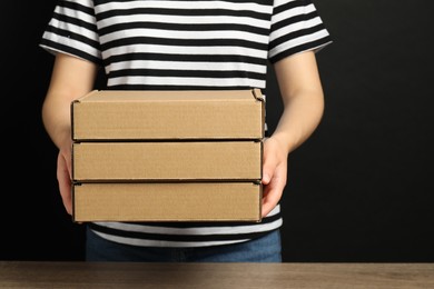 Photo of Woman holding cardboard boxes on black background, closeup. Packaging goods