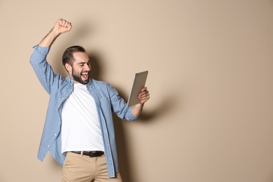 Emotional young man with tablet celebrating victory on color background. Space for text