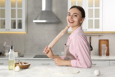 Photo of Smiling woman with soiled face holding rolling pin at messy table in kitchen