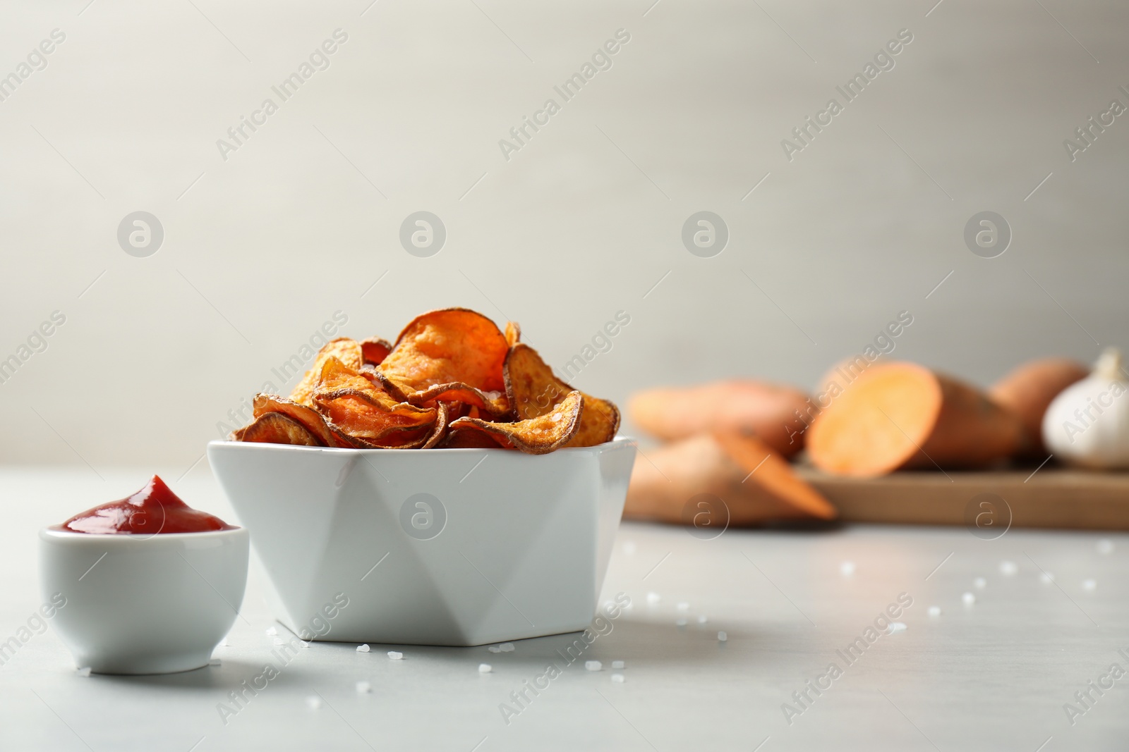 Photo of Delicious sweet potato chips in bowl and sauce on table. Space for text