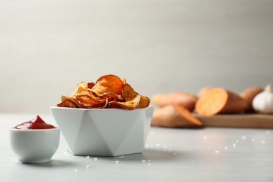 Delicious sweet potato chips in bowl and sauce on table. Space for text