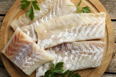 Fresh raw cod fillets and parsley on wooden table, top view