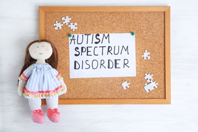 Photo of Sheet of paper with words AUTISM SPECTRUM DISORDER and doll on cork board
