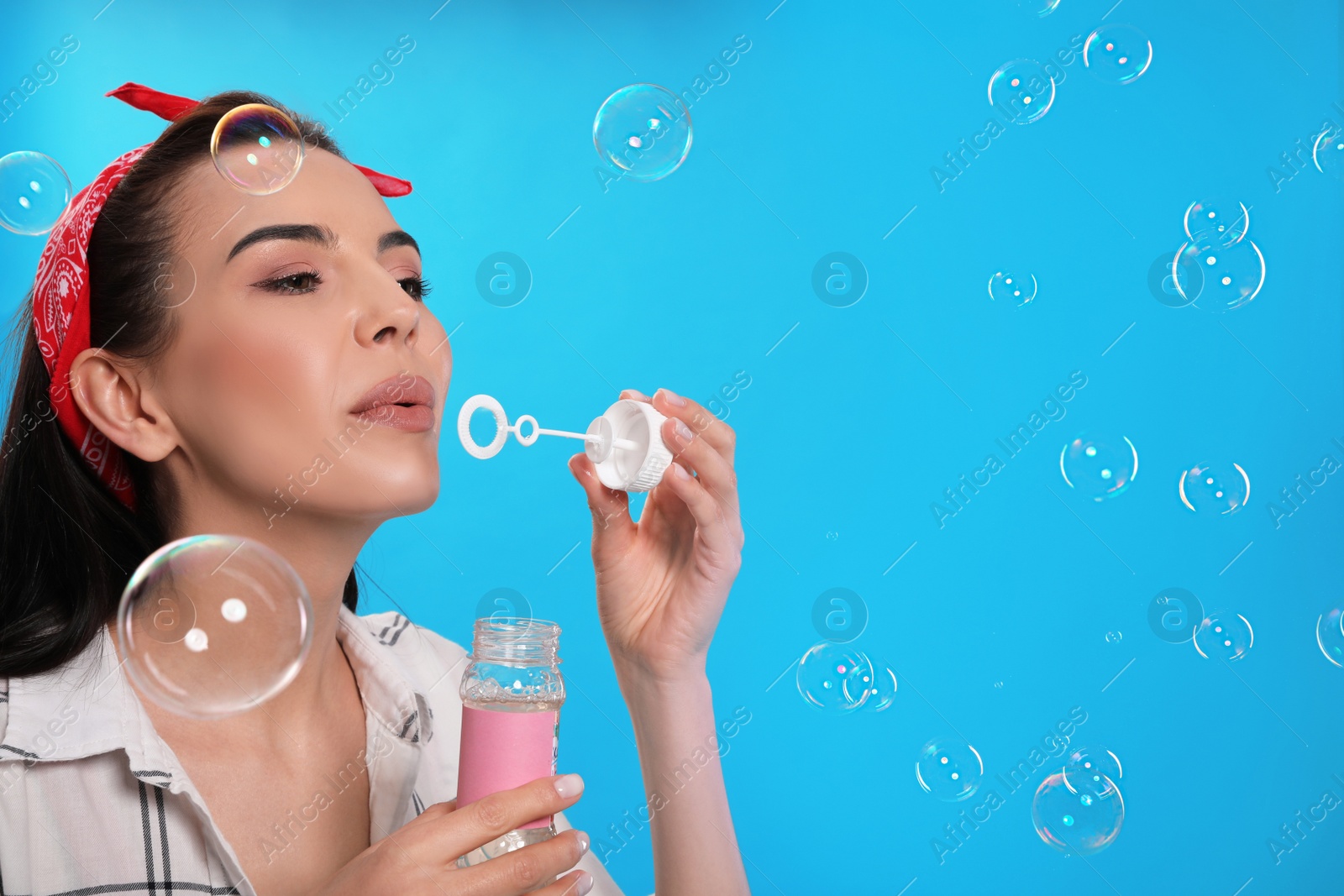 Photo of Young woman blowing soap bubbles on light blue background, space for text