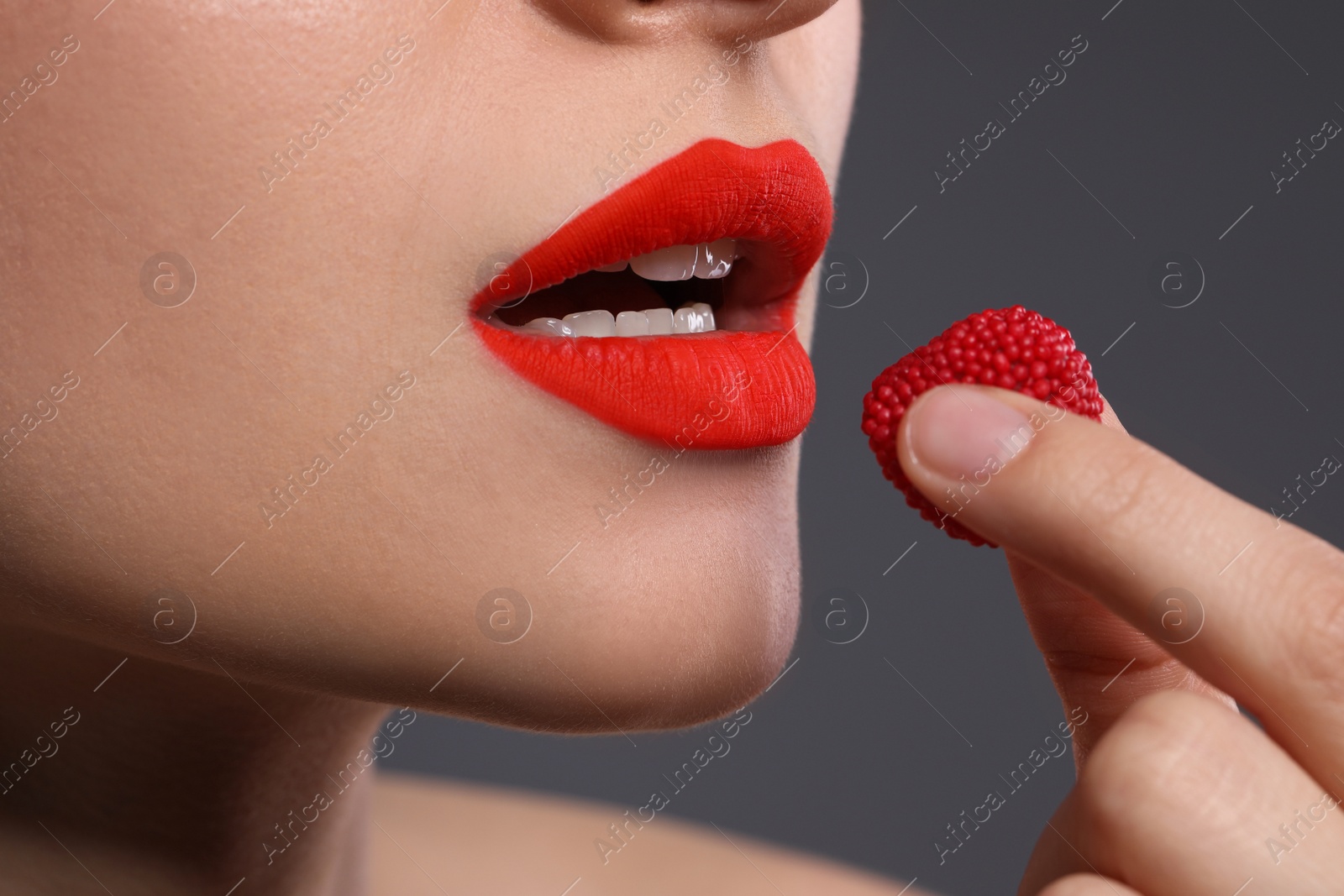 Photo of Young woman with beautiful red lips makeup eating candy on grey background, closeup