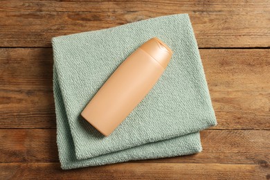 Photo of Soft folded terry towel and cosmetic bottle on wooden table, top view