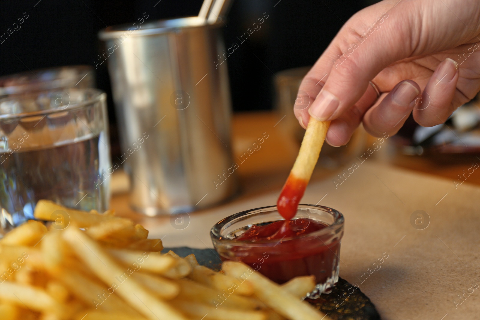 Photo of Woman dipping French fries into red sauce in cafe, closeup