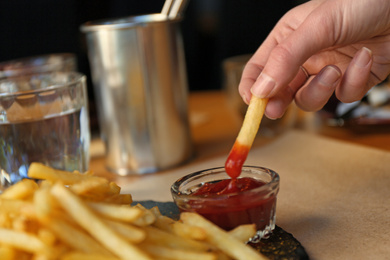 Photo of Woman dipping French fries into red sauce in cafe, closeup