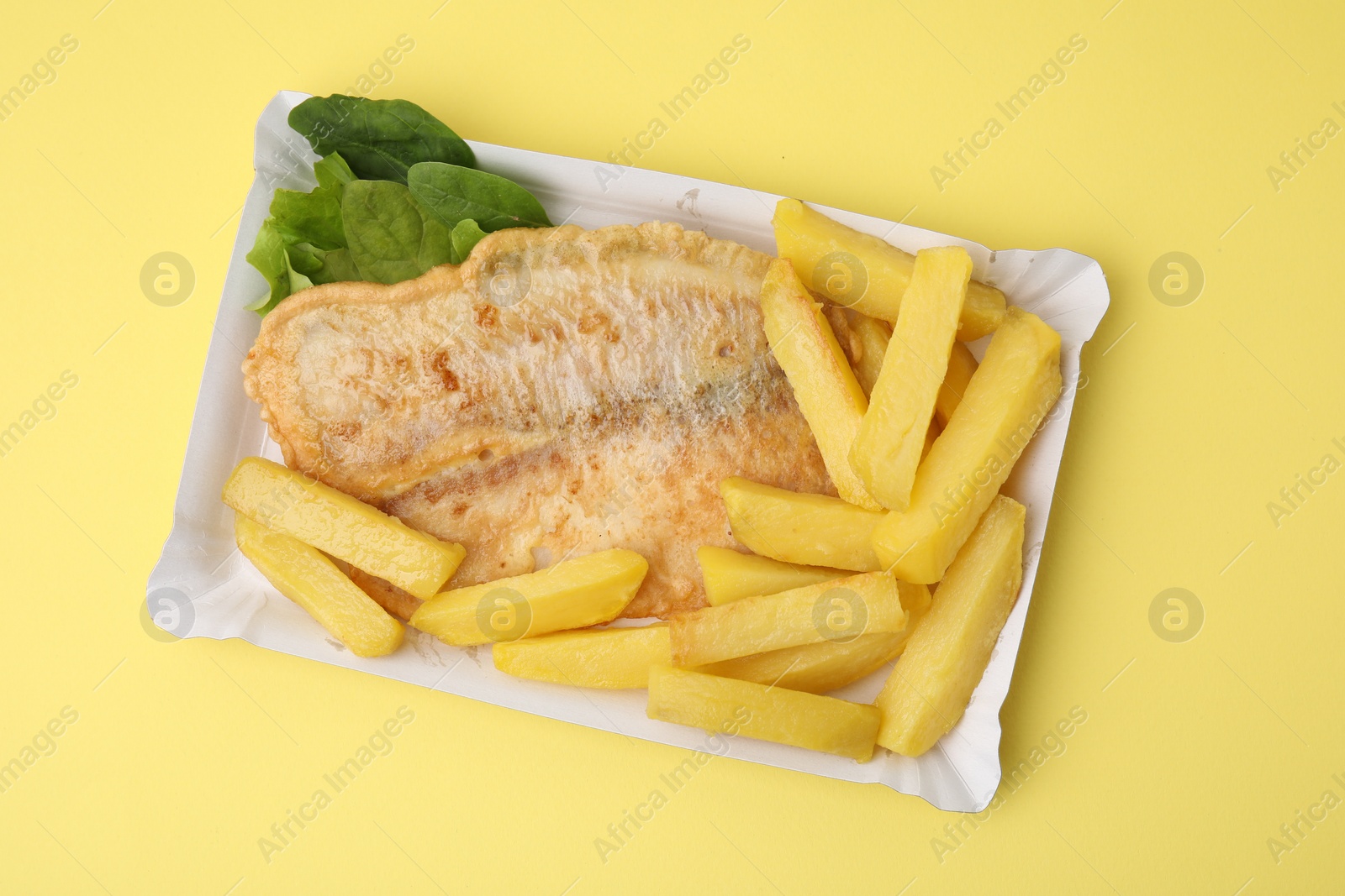 Photo of Delicious fish and chips with spinach and lettuce on yellow table, top view