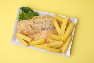 Photo of Delicious fish and chips with spinach and lettuce on yellow table, top view