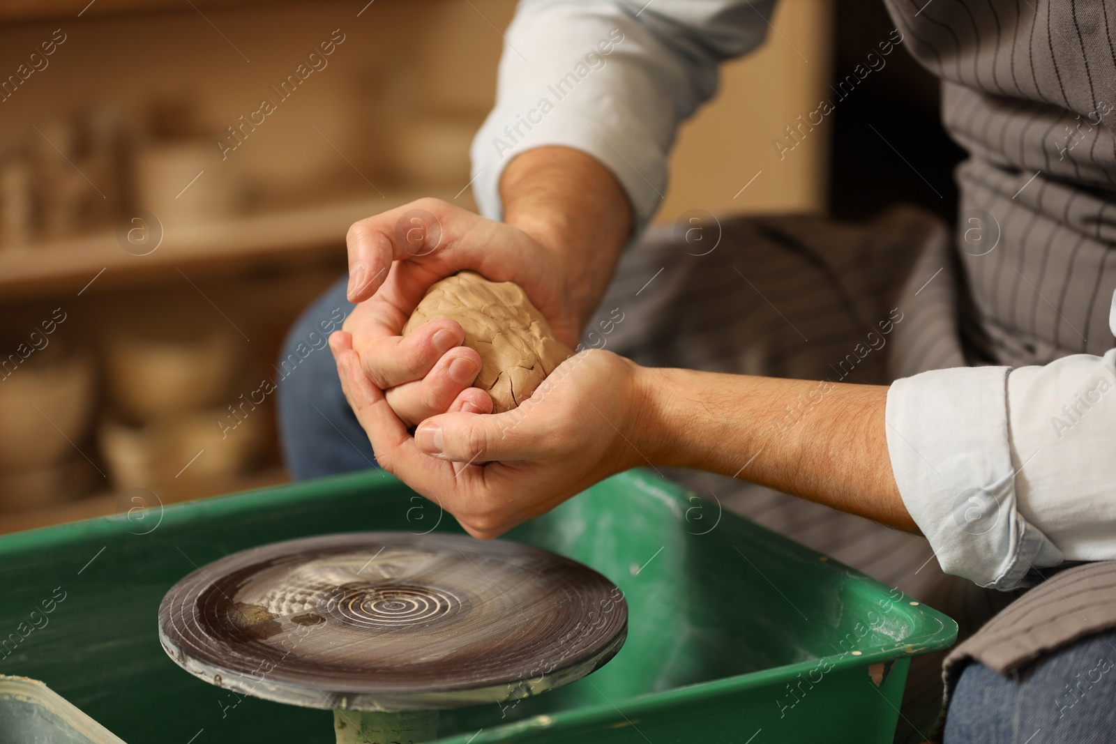 Photo of Man crafting with clay over potter's wheel indoors, closeup