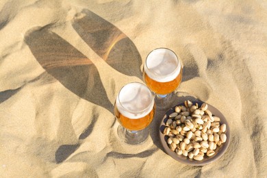 Photo of Glasses of cold beer and pistachios on sandy beach, above view