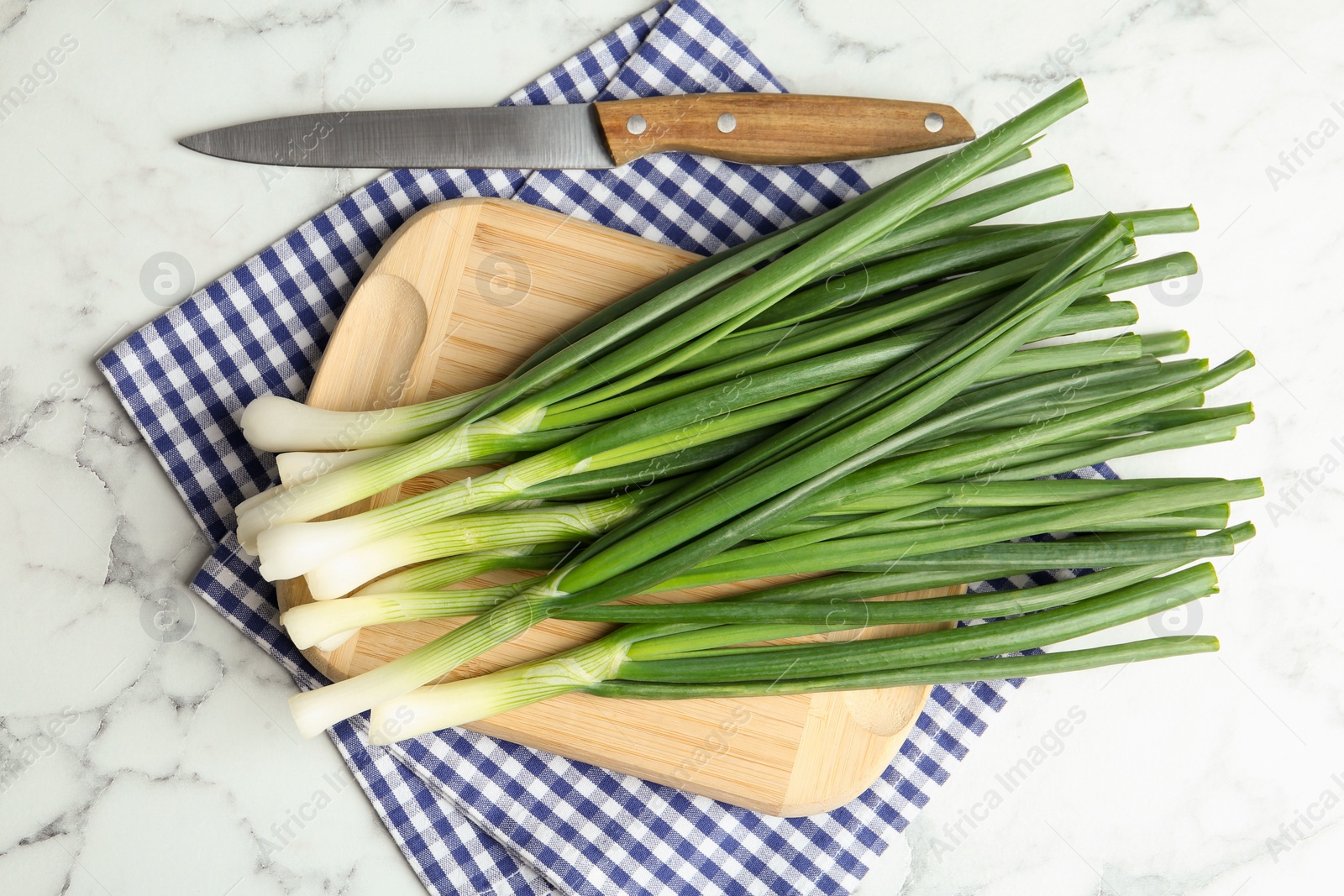 Photo of Fresh green spring onions, knife and cutting board on white marble table, flat lay