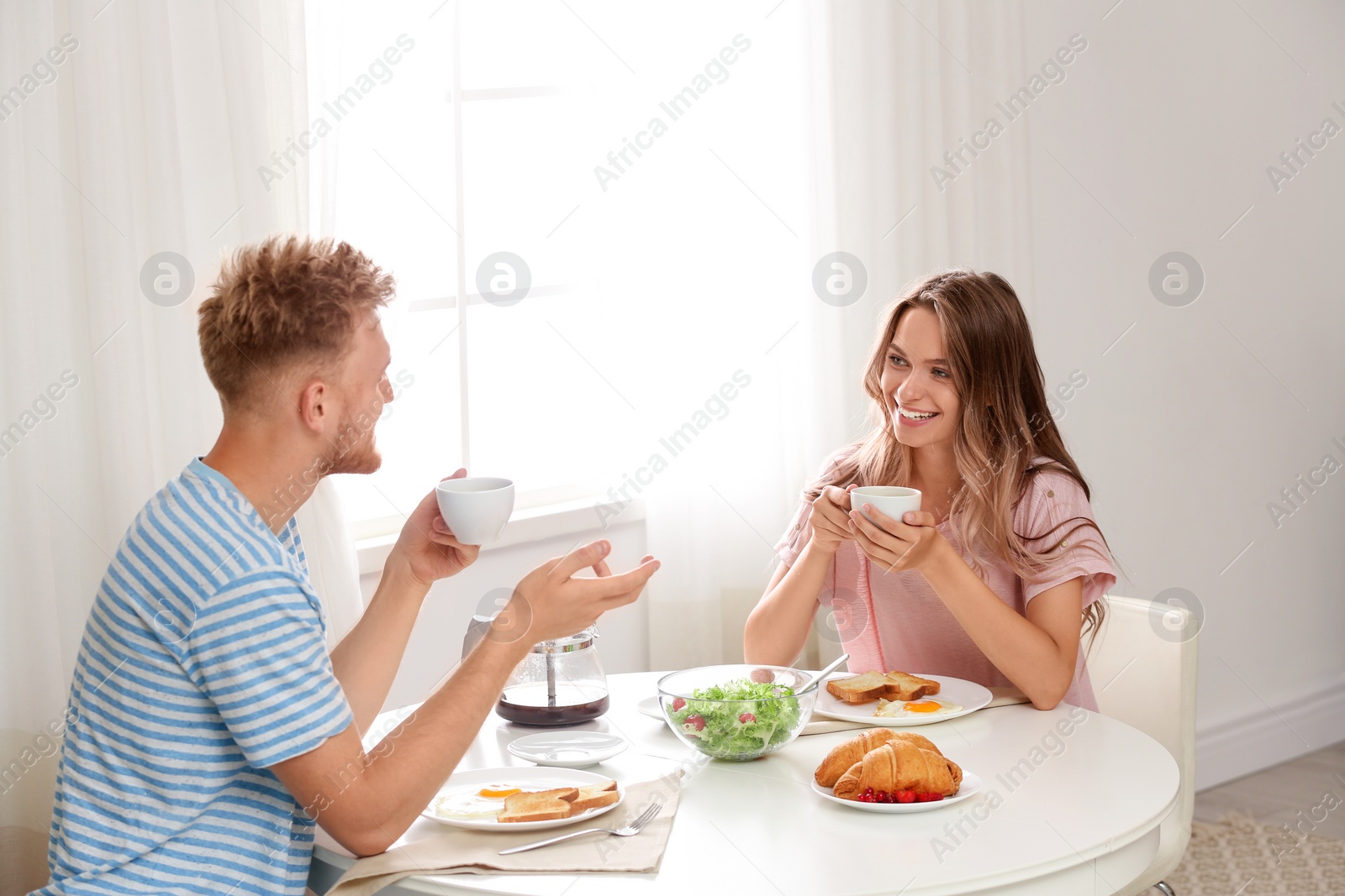 Photo of Happy young couple having breakfast at table in room