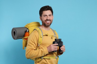Photo of Happy man with backpack and binoculars on light blue background, space for text. Active tourism