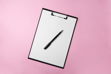 Photo of Black clipboard with sheet of blank paper and pen on pink background, top view