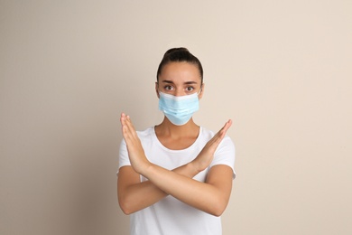 Photo of Woman in protective mask showing stop gesture on beige background. Prevent spreading of COVID‑19