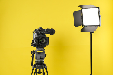 Photo of Professional video camera and lighting equipment on yellow background