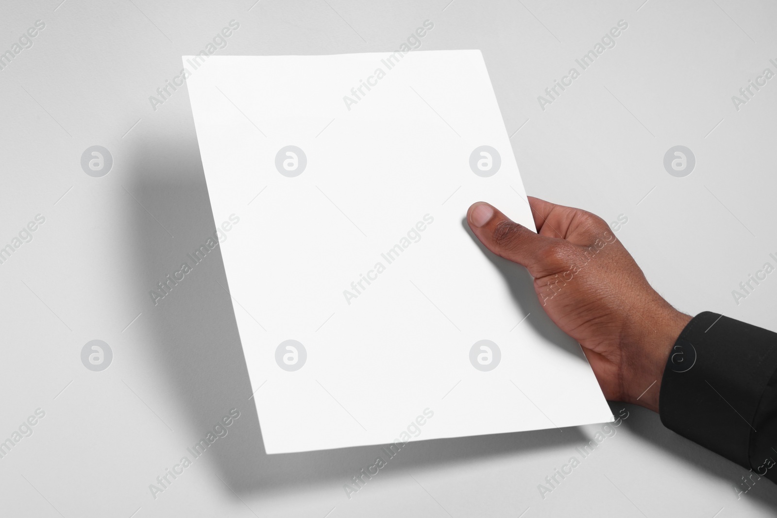 Photo of African American man holding sheet of paper on white background, closeup. Mockup for design