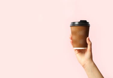 Woman holding takeaway paper coffee cup on pink background, closeup