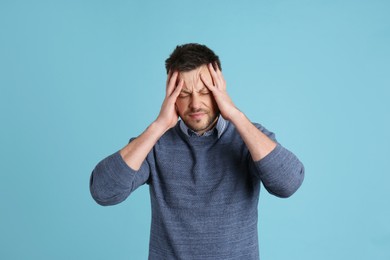 Photo of Man suffering from terrible migraine on light blue background