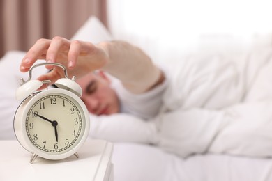 Man turning off alarm clock in bedroom, focus on hand. Space for text