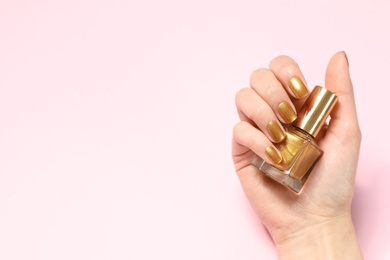 Photo of Woman holding bottle of golden nail polish in manicured hand on color background, top view. Space for text