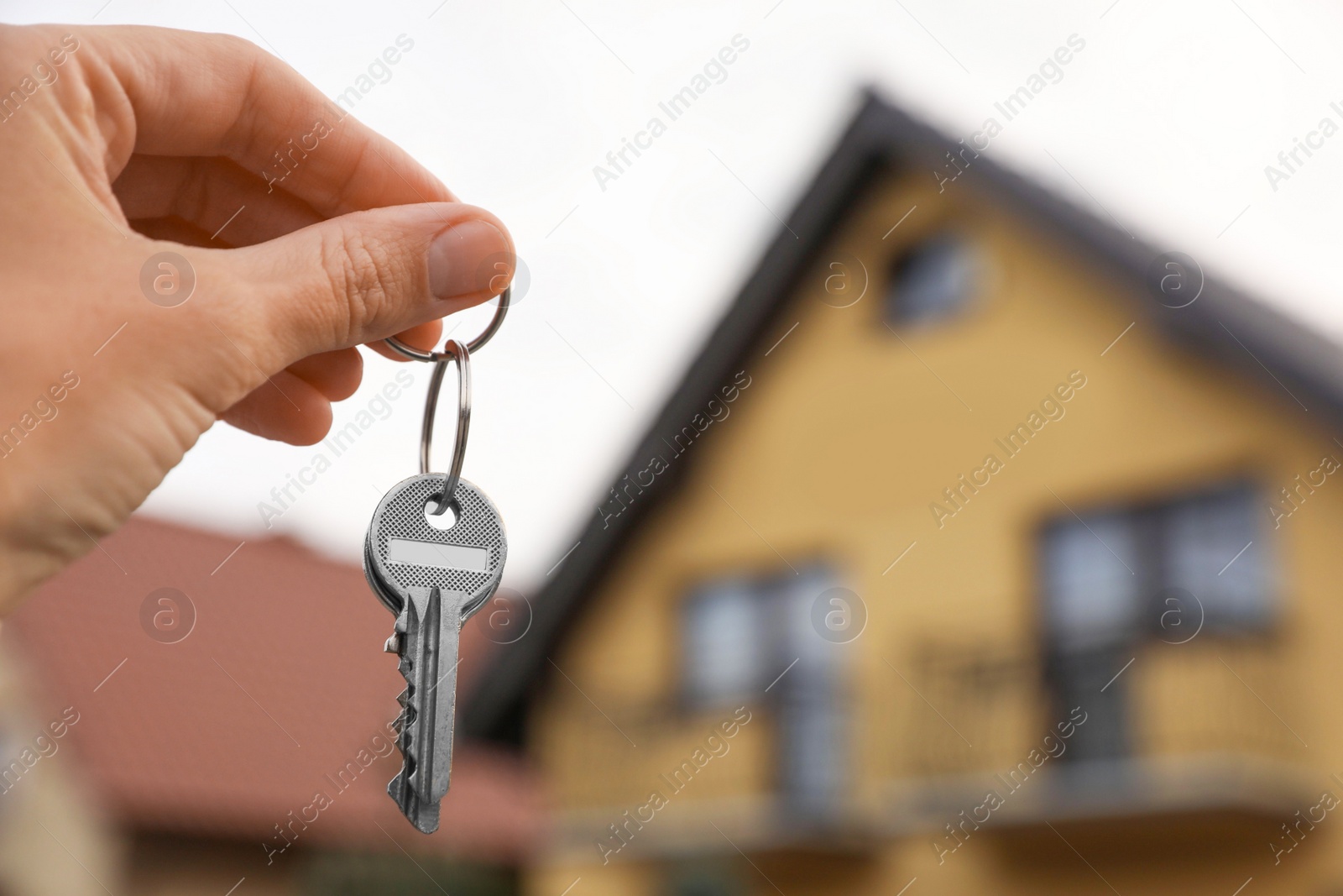 Photo of Real estate agent holding keys to new house outdoors, closeup. Space for text