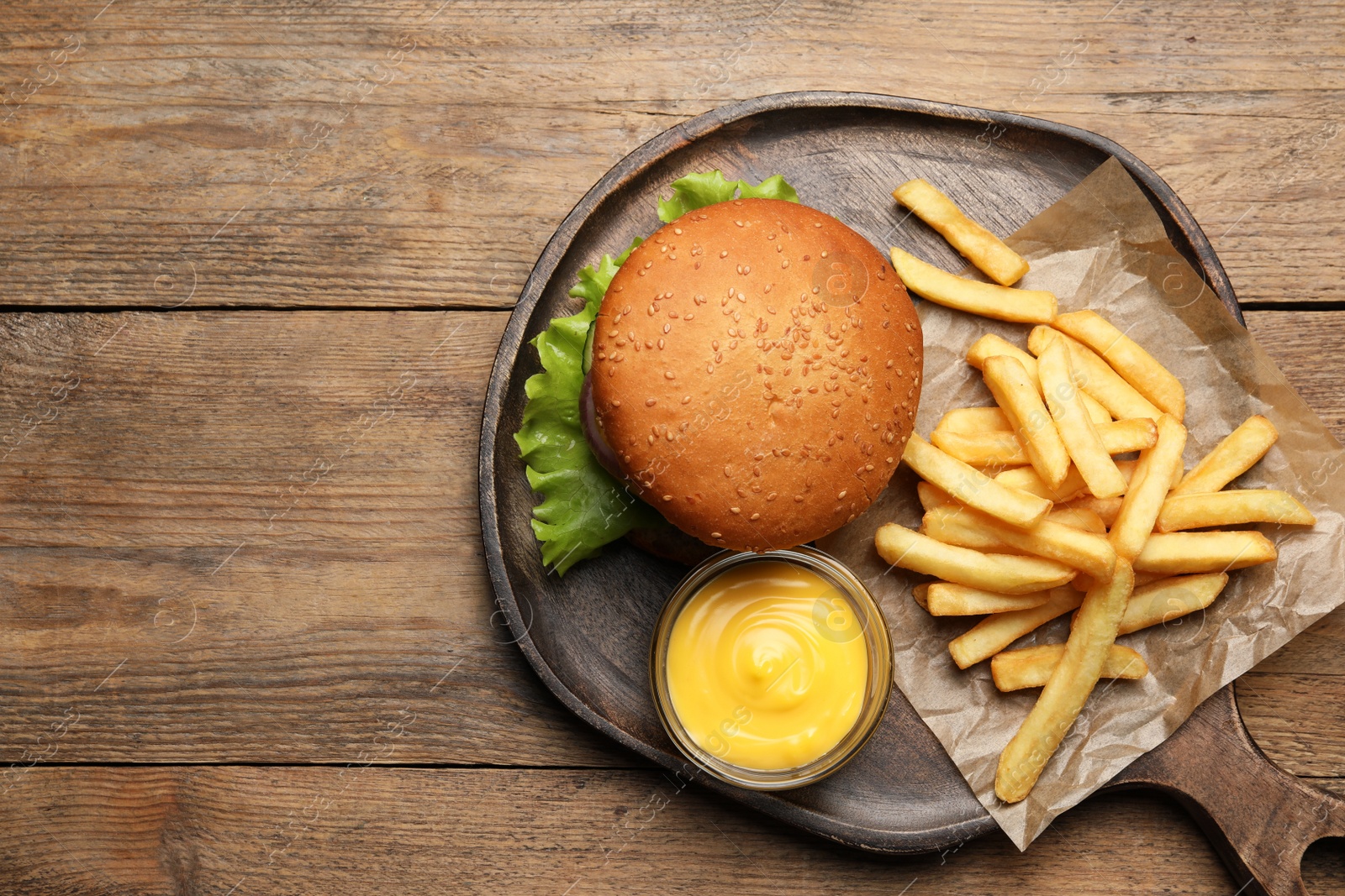 Photo of French fries, tasty burger and sauce on wooden table, top view. Space for text