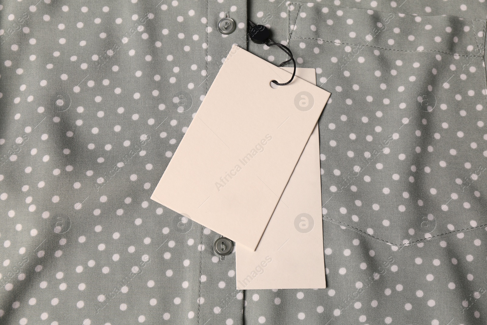 Photo of Blank white tags on grey shirt with polka dot pattern, top view. Space for text