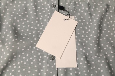 Photo of Blank white tags on grey shirt with polka dot pattern, top view. Space for text