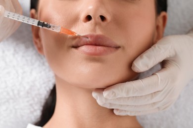 Photo of Doctor giving lips injection to young woman in clinic, top view. Cosmetic surgery
