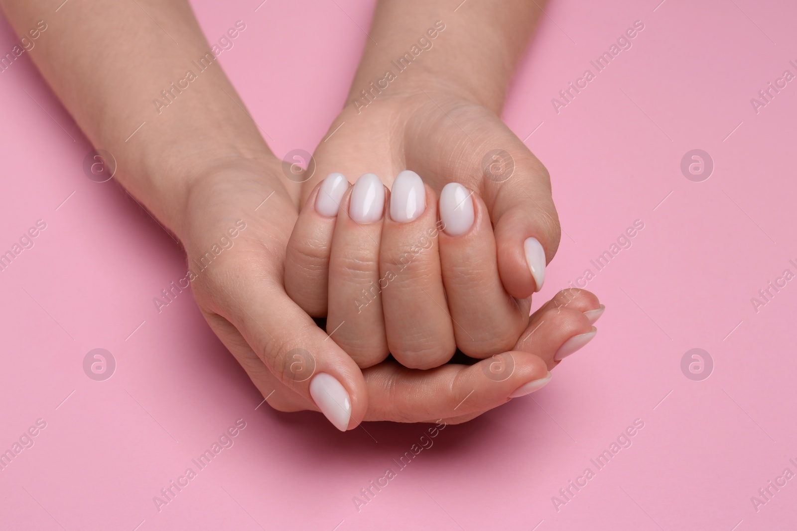 Photo of Woman showing her manicured hands with white nail polish on pink background, closeup