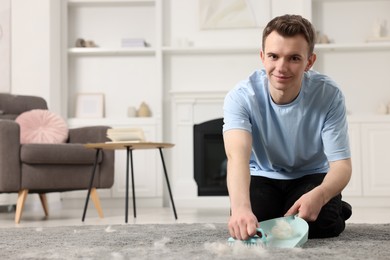 Photo of Man with brush and pan removing pet hair from carpet at home. Space for text