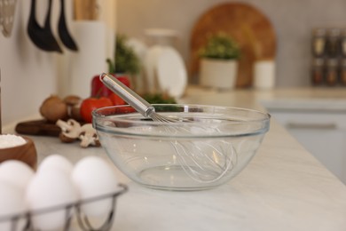 Metal whisk, bowl and different products on light table in kitchen