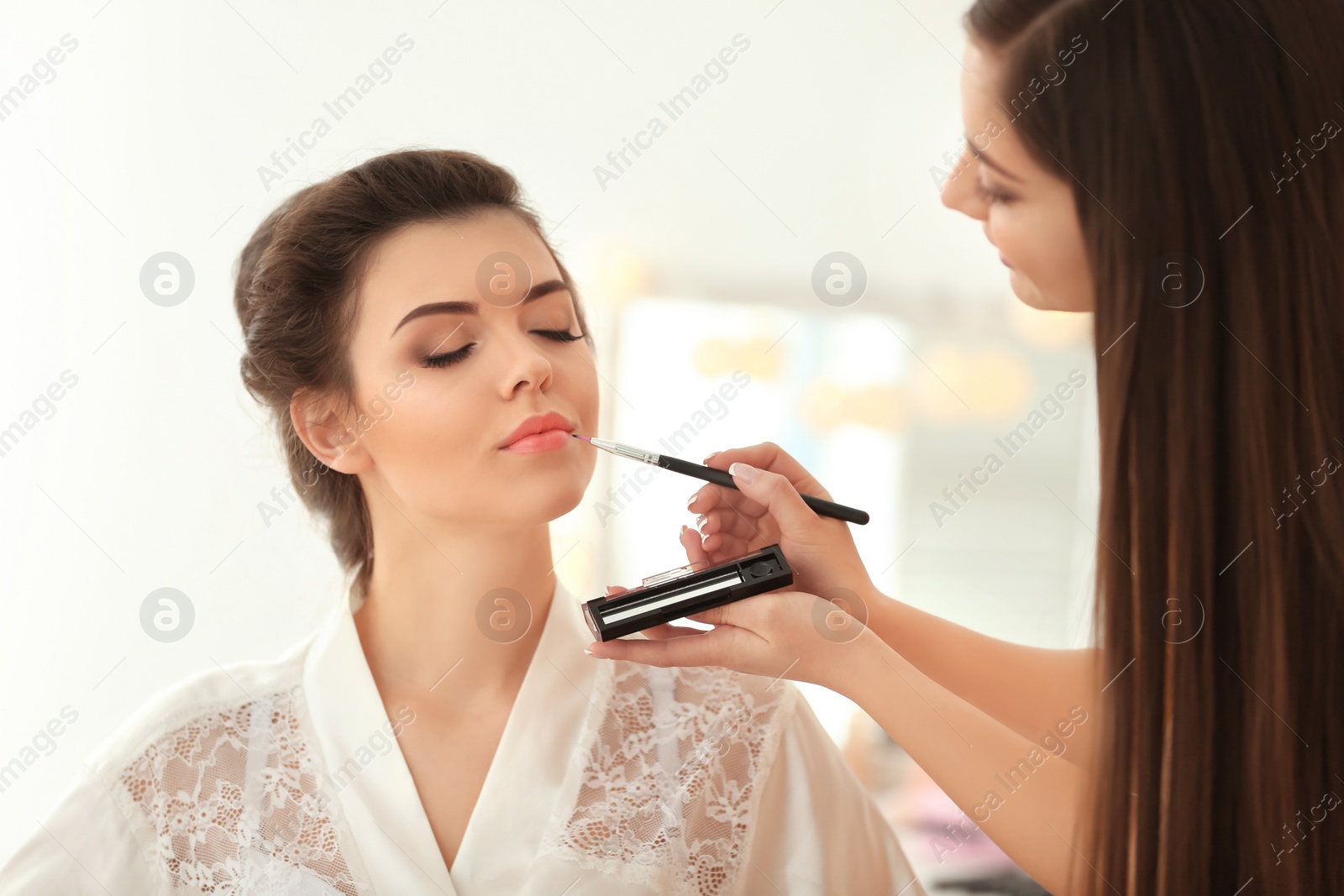 Photo of Makeup artist preparing bride before her wedding in room