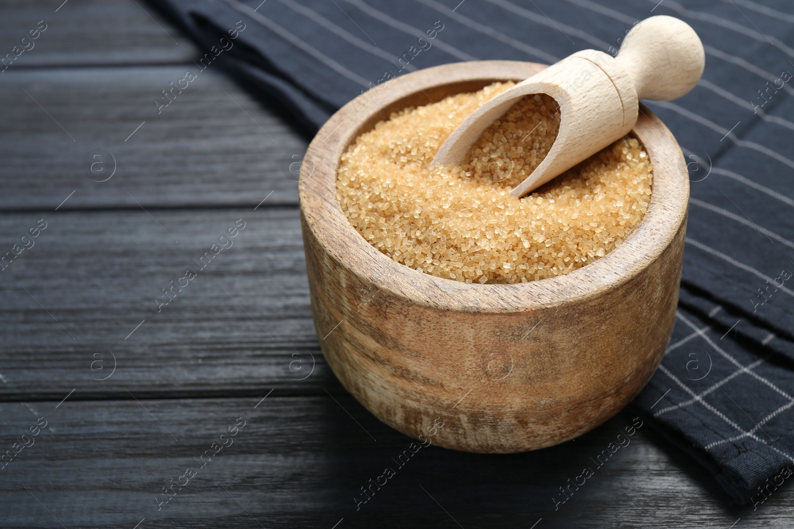 Photo of Brown sugar in bowl and scoop on black wooden table, closeup. Space for text