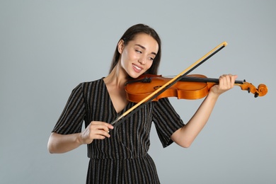 Beautiful woman playing violin on grey background