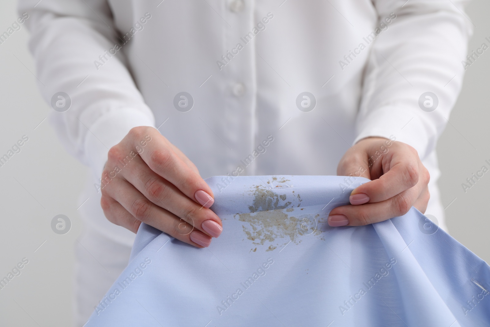 Photo of Woman holding shirt with stain against light background, closeup