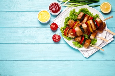 Photo of Delicious chicken shish kebabs with vegetables and sauce on light blue wooden table, flat lay. Space for text