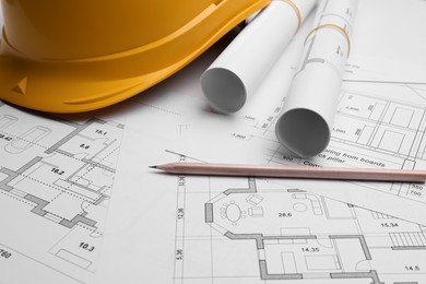 Photo of Blueprints, hardhat and pencil on white table, closeup