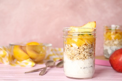 Tasty peach dessert with yogurt and granola served on pink wooden table. Space for text