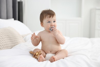 Photo of Cute baby boy with pacifier and wooden rattle on bed at home