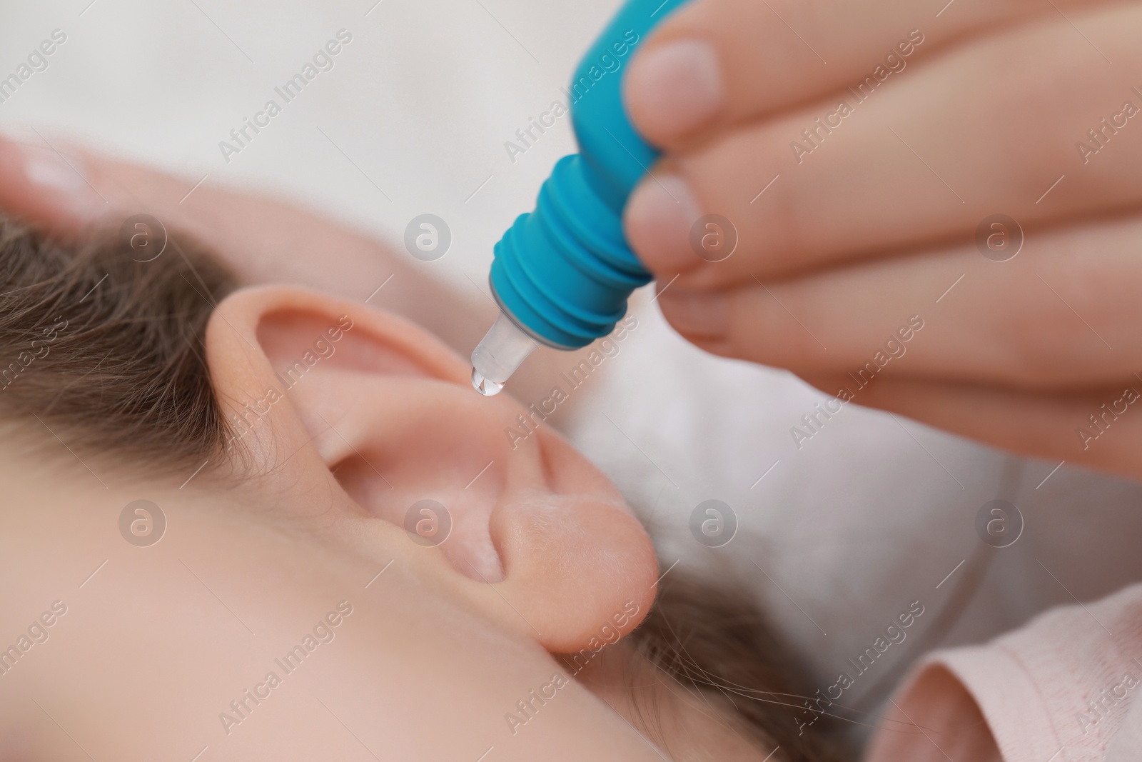 Photo of Mother dripping medication into daughter's ear on light background, closeup