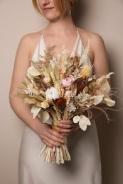 Photo of Bride holding beautiful dried flower bouquet on beige background, closeup