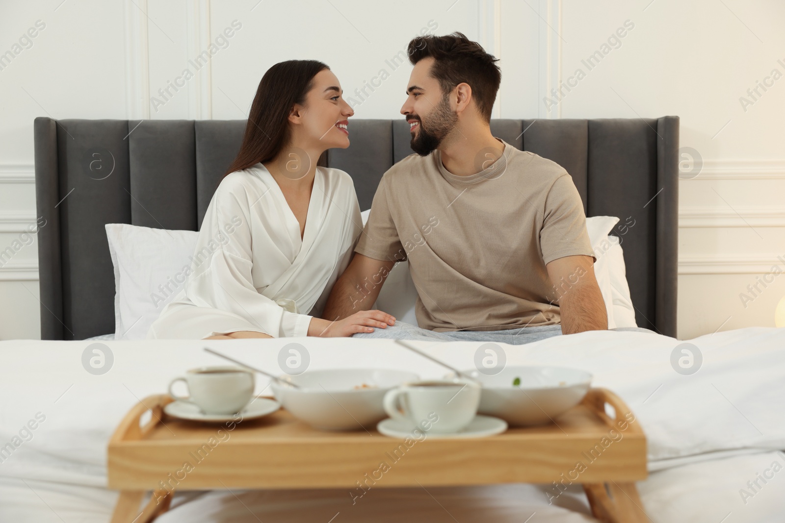 Photo of Happy couple together near wooden tray with breakfast on bed at home