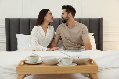 Happy couple together near wooden tray with breakfast on bed at home